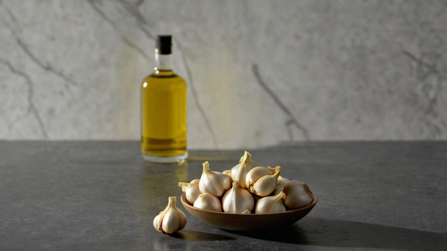 Fresh garlic cloves and a small bowl of oil on a clean kitchen counter
